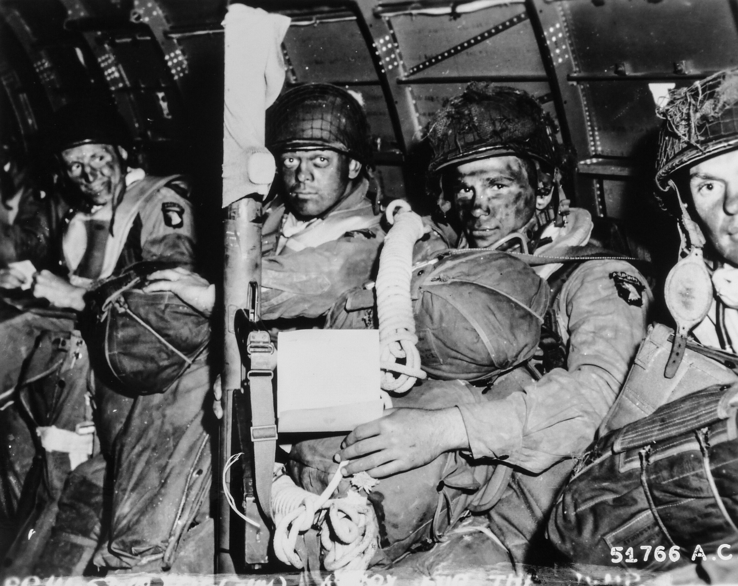 American paratroopers seated in a transport aircraft before takeoff on D-Day, the man in front holding General Eisenhower Order of the Day